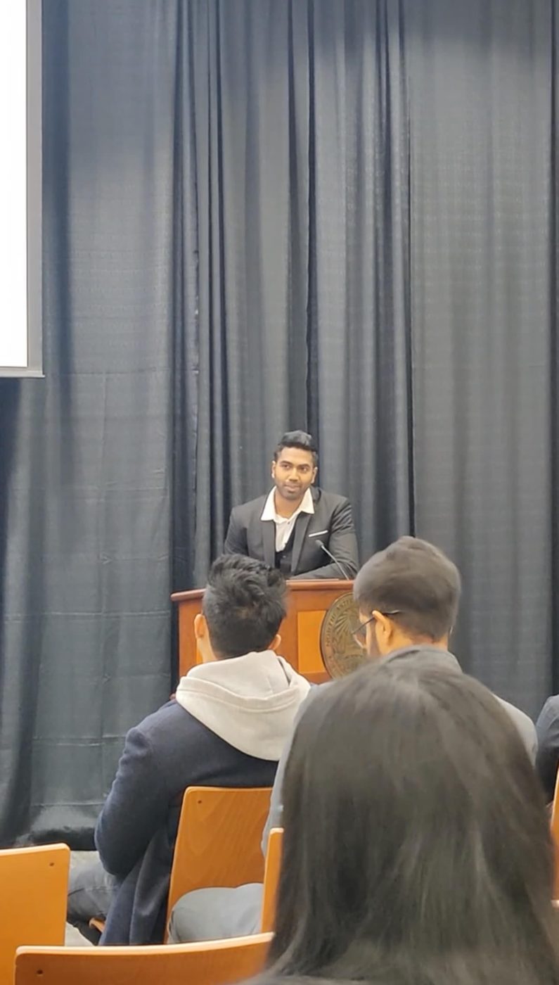 Rajaseelan speaking at a podium at Northeastern University